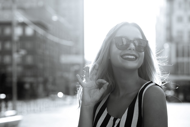 Glamor cheerful model in glasses showing ok gesture, enjoying summer day. Empty space. Black and white toning