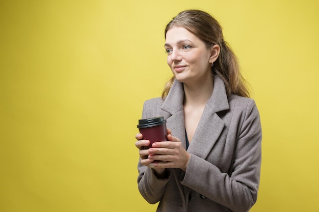 Donna glamour con gli occhiali in un maglione arancione con una bevanda di caffè su sfondo giallo