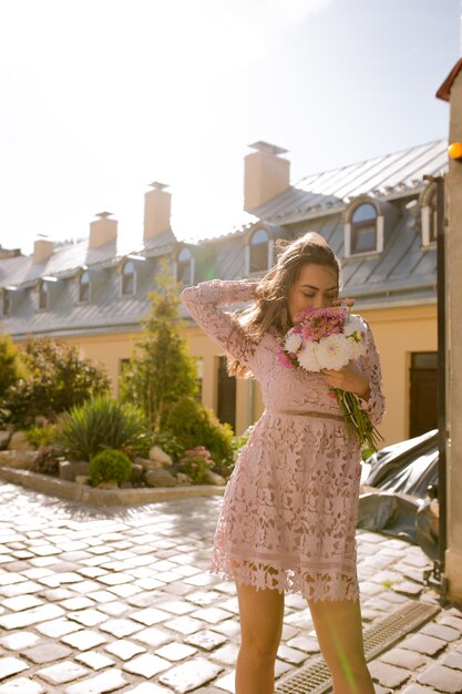 Glamor young model with fluttering hair holding bouquet of flowers. Woman posing in sunny day