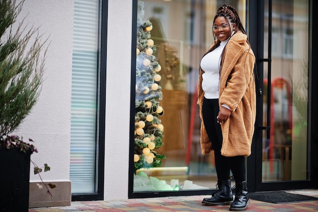 Glamorous african american woman in warm fur coat pose at street near christmas tree