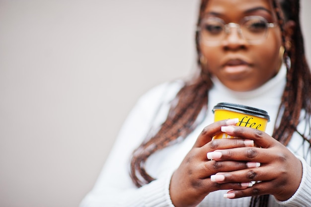 Glamorous african american woman in white turtleneck sweater pose at street with cup of coffee at hand