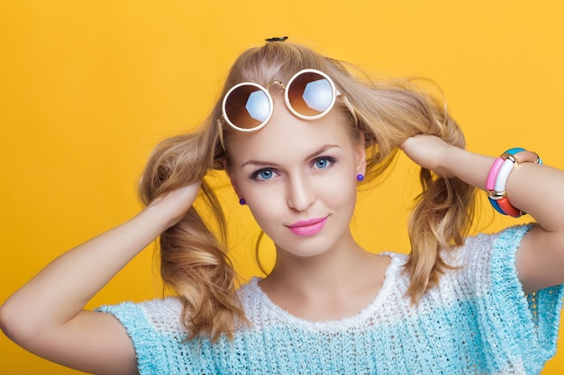 Glamorous beautiful blond woman in sunglasses and blue shirt on yellow background happy summer time