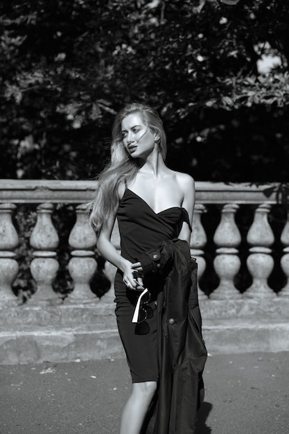 Glamorous blonde woman with long hair wearing dress, takes off her coat. Monochrome toning