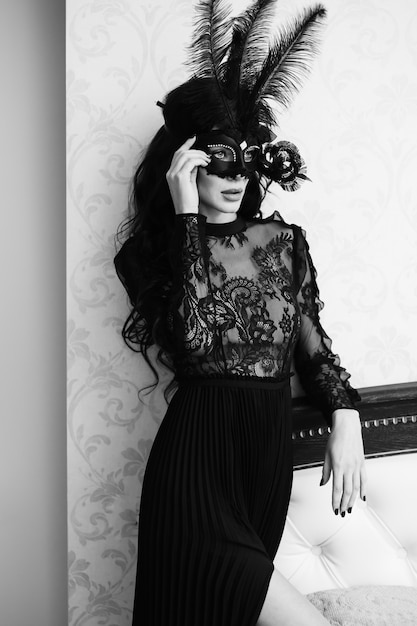 Glamorous brunette lady with a beautiful hairstyle and red lips, in an evening dress, a venetian black mask with stylish accessories