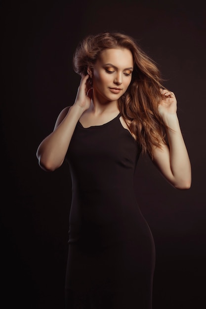 Glamorous brunette model in black dress with fluttering hair with wind