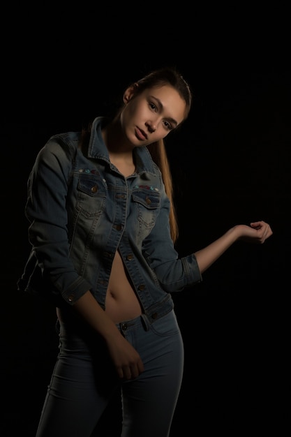 Glamorous brunette woman in trendy jeans jacket posing at black background