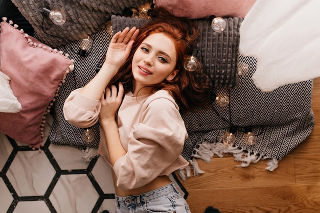 Glamorous ginger girl lying on the floor Overhead portrait of stunning female model posing at home