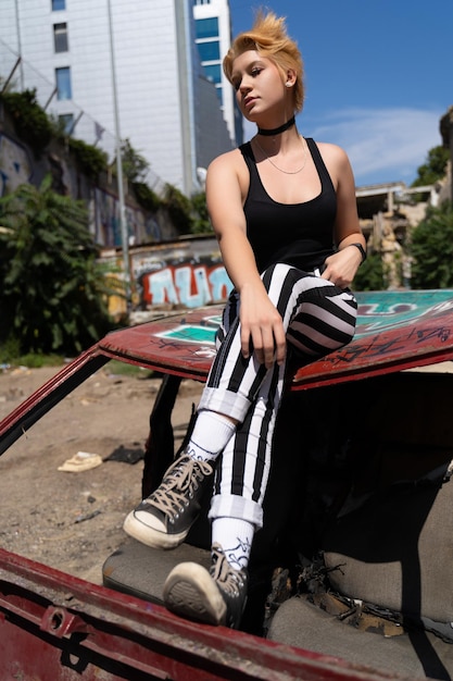 Glamorous girl in pants and short hair and makeup posing near a broken old car