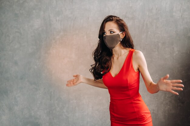 Glamorous girl in a red dress and a protective mask on a vintage background