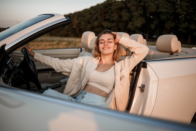 Photo a glamorous luxury girl with blonde hair smiling while sitting on a white convertible. young successful woman sitting in her white car