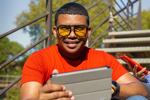 Photo glamorous smiling young man sitting using a app on a digital tablet outdoors