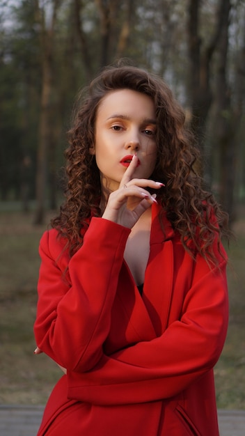 Гламурная женщина в красном наряде и соответствующем красном блеске для губ. портрет в парке