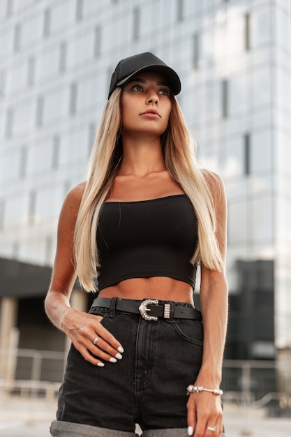 glamorous young model woman in black jeans fashion clothes with black cap walks in the city