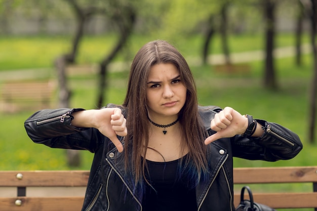 Photo glamorous young woman in black leather jacket sitting in the park on the bench