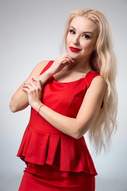 Glamorous young woman in red dress on gray background