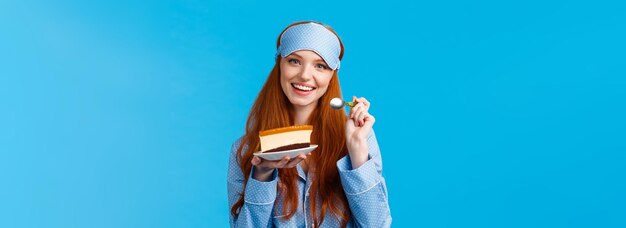 Glamour aantrekkelijk roodharige blanke vrouw in nachtwee slaapmasker die heerlijke cake eet met ta