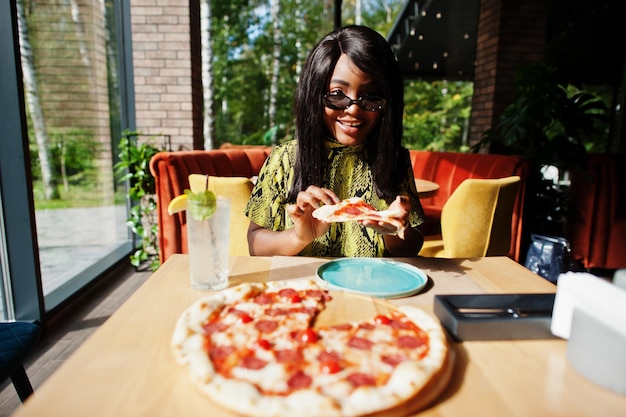 Glamour african american woman eating pizza at restaurant.