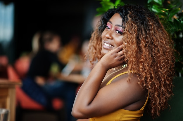 Glamour Afro-Amerikaanse vrouw in gele jurk gesteld in restaurant.