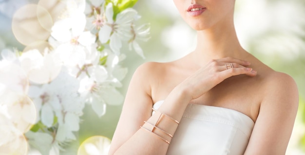 glamour, beauty, jewelry and luxury concept - close up of beautiful woman with golden ring and bracelet over natural spring cherry blossom
