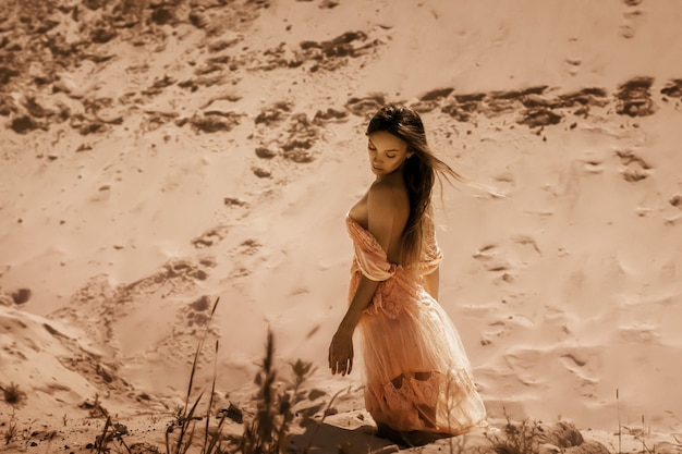 매력적인 갈색 머리 아가씨는 사막의 모래에 앉아