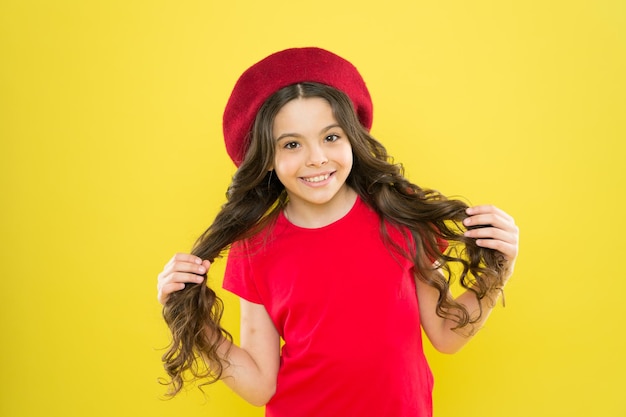 グラマーガールモデルパリジャン子供黄色の背景夏のファッションと美容子供時代の美容院サロンベレー帽の長い巻き毛の幸せな女の子フレンチスタイルの帽子の小さな女の子