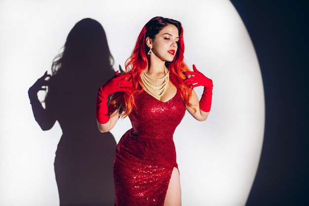 Glamour lady in red dress is posing on camera in studio background