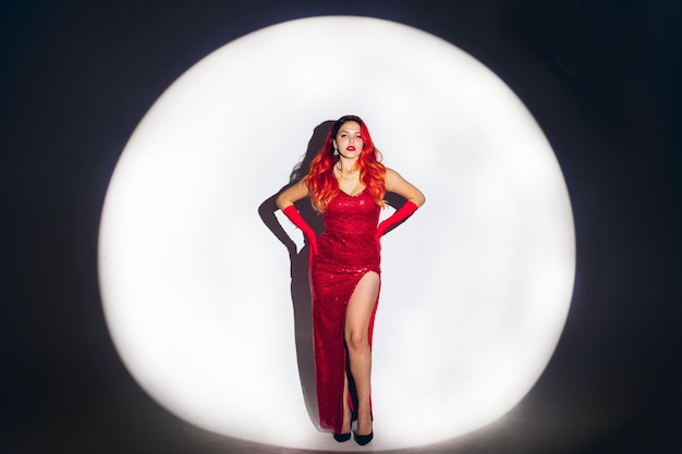 Glamour lady in red dress is posing on camera in studio background