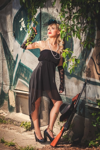 Glamour model standing in front of stone wall with graffiti near gun