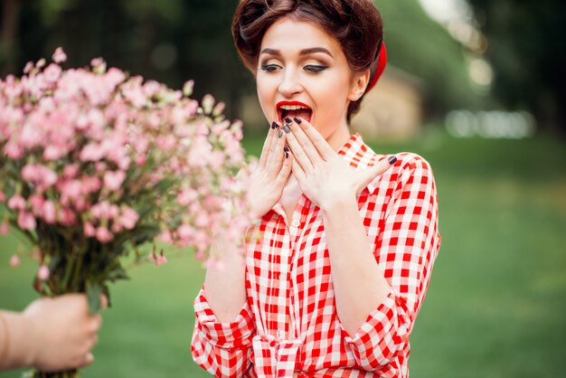 Glamour pinup girl takes gift a bouquet of flowers, retro american fashion. Attractive woman in pin up style