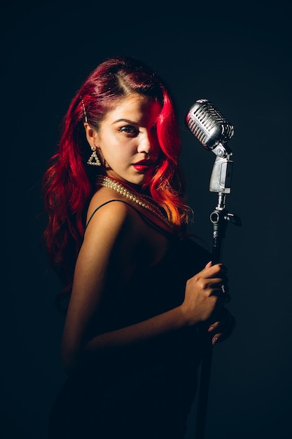 Glamour red haired lady singing with microphone on the dark stage background