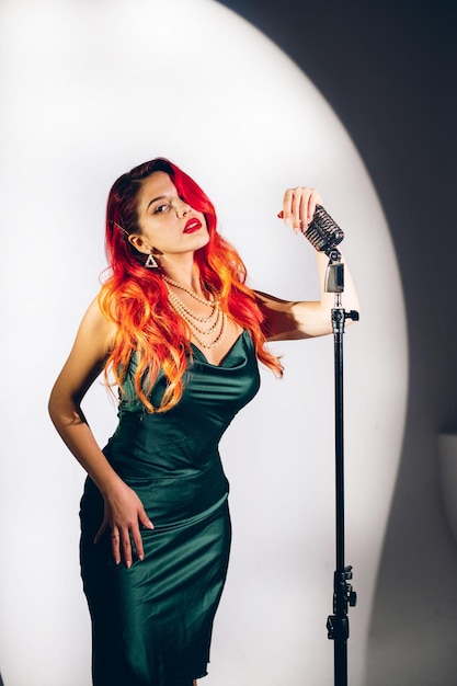 Photo glamour red haired lady singing with microphone on the dark stage background