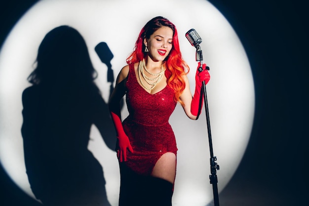 Glamour red haired lady singing with microphone on the dark stage background
