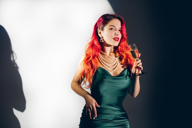 Glamour red haired woman holding a glass of champagne on the contrast background