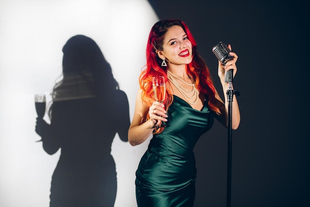 Photo glamour red haired woman holding a glass of champagne on the contrast background