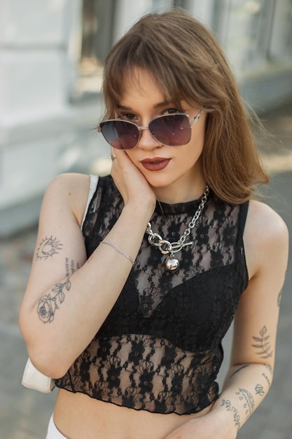 Гламурная сексуальная модная красотка в солнечных очках в черном стильном кружевном топе с сумкой ходит по улице