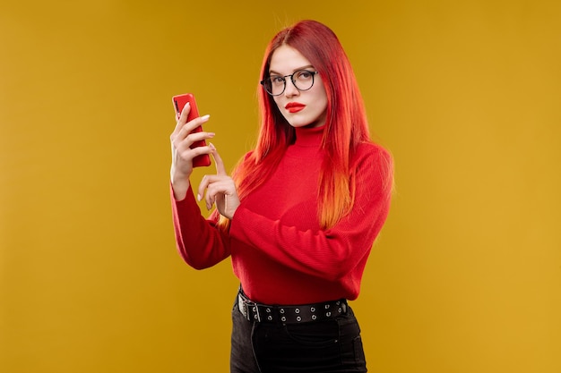 Glamour vrouw die een bril draagt die smartphone op gele achtergrond gebruikt