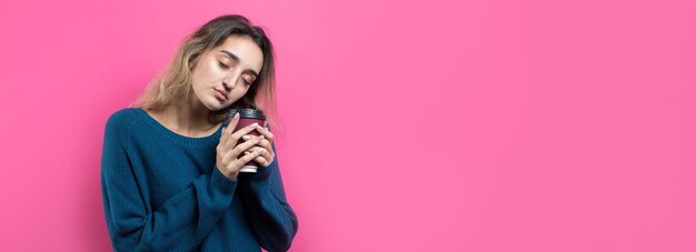 Glamour vrouw in bril in een blauwe trui met een drankje van koffie op een roze achtergrond