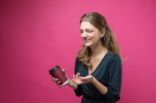 Glamour vrouw in een donkerblauwe jurk met een drankje van koffie op een roze achtergrond