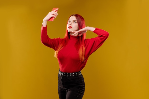 Glamour woman with red hair using smartphone on yellow background