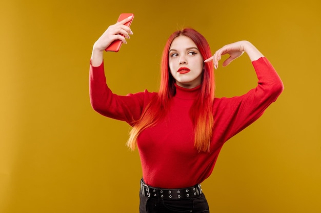 Гламурная женщина с рыжими волосами с помощью смартфона на желтом фоне