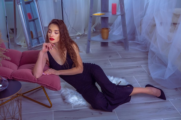 Glamour woman with red lips in black overalls sits on the floor at home