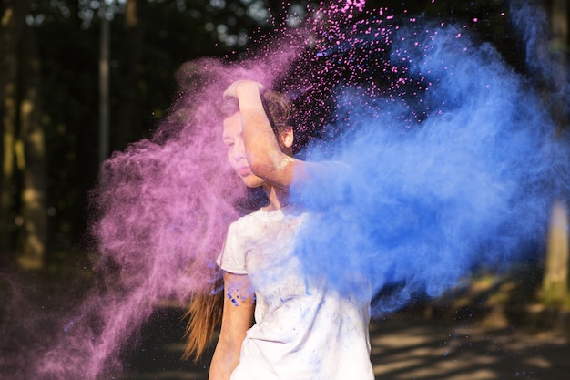 Glamoureuze gebruinde jonge vrouw die een wit t-shirt draagt, speelt met de kleurrijke verf van Holi