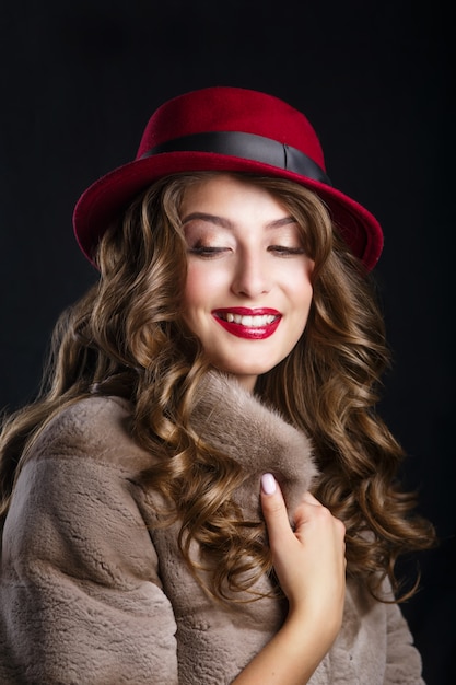 Glamourportret van mooi vrouwenmodel met rode lippen en lang donkerbruin haar in luxebontjas en hoedenkleur marsala