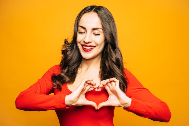 Glanzend meisje met een perfecte huid, lang glad en krullend haar en een fluwelen rode lippenstift op haar volle lippen draagt een rode bijpassende trui voor een vlammende achtergrond