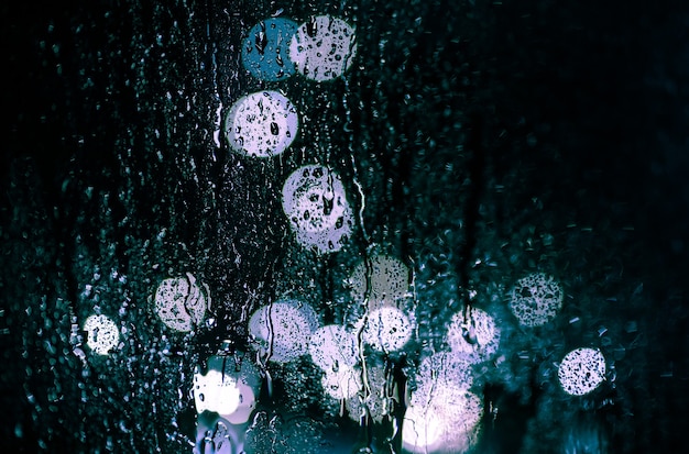Il bagliore della città notturna attraverso la finestra nelle gocce di pioggia