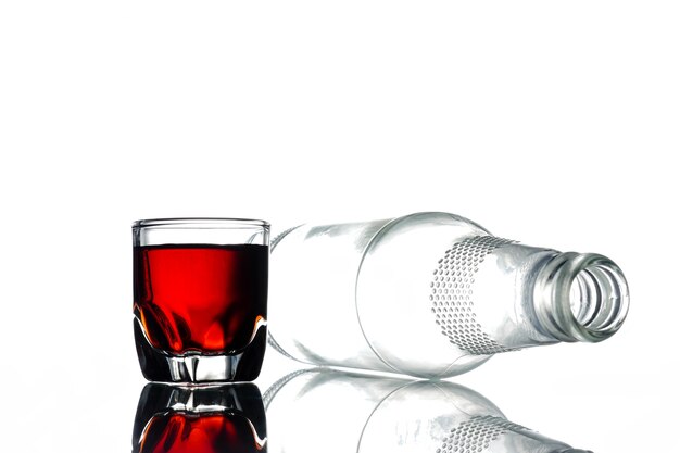 Glas alcohol en lege fles op een witte achtergrond.