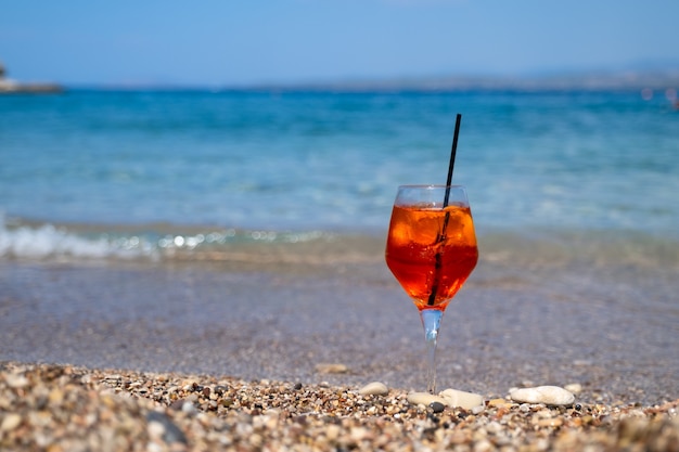 Glas aperol spritz cocktail staat op zand in de buurt van de zee