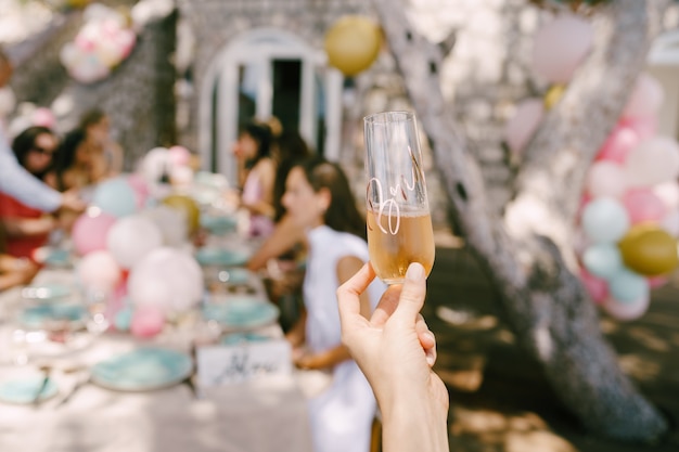 Glas champagne in de hand tegen de achtergrond van een geserveerde tafel met gasten