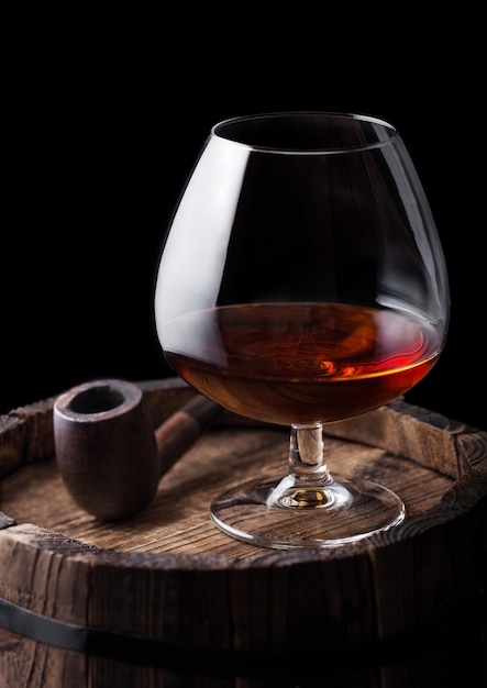 Glas cognac cognacdrank en vintage rookpijp bovenop houten vat