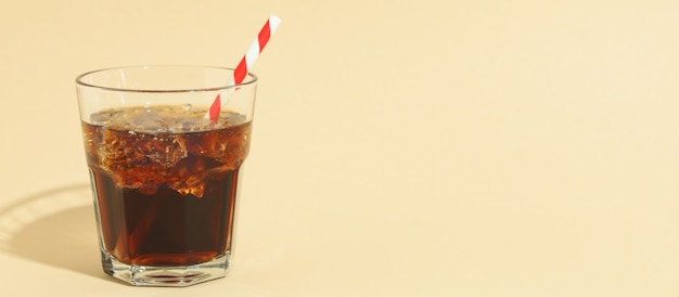 Glas cola met ijsblokjes en stro op beige oppervlak